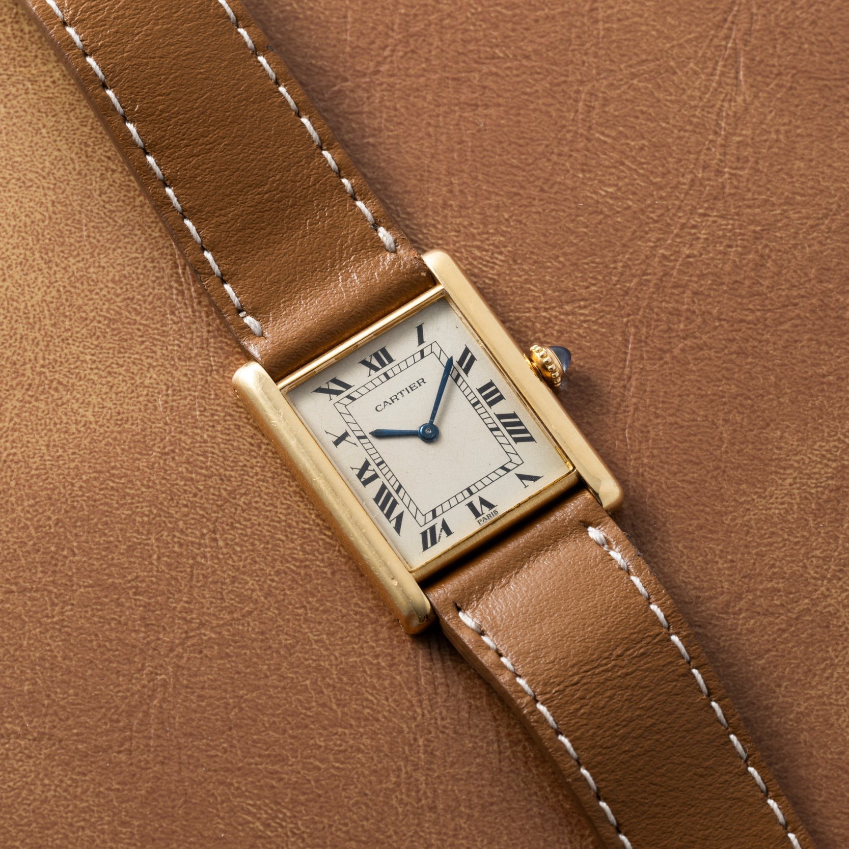 A Cartier Tank Louis watch with a brown leather strap rests on a matching brown leather surface.
