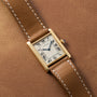 A Cartier Tank Louis watch with a brown leather strap rests on a matching brown leather surface.