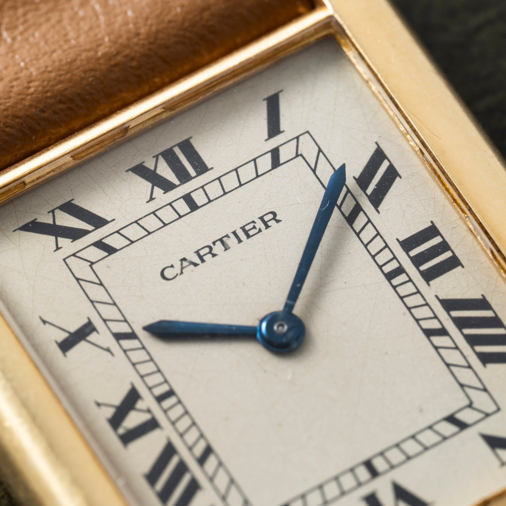 Close-up of a Cartier Tank Louis watch face with Roman numerals and blue hands in a gold rectangular frame.