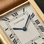 Close-up of a Cartier Tank Louis watch face with Roman numerals and blue hands in a gold rectangular frame.