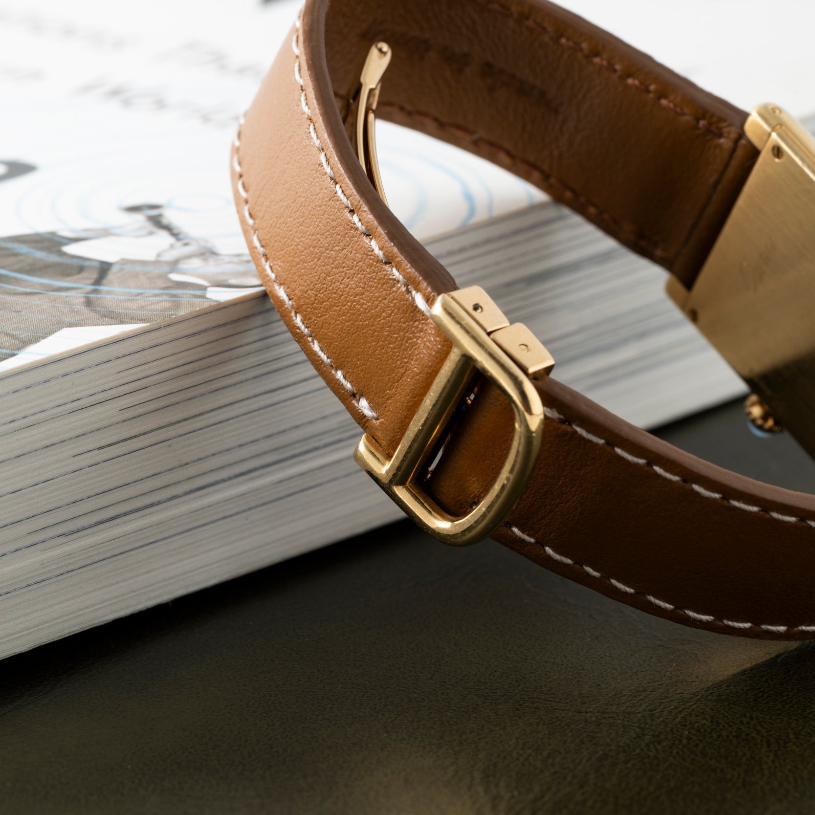 Close-up of a Cartier Tank Louis brown leather watch strap resting on the edge of a white book.