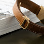 Close-up of a Cartier Tank Louis brown leather watch strap resting on the edge of a white book.