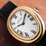 Cartier Baignoire watch with Roman numerals, black leather strap, and blue hands displayed on a brown surface.