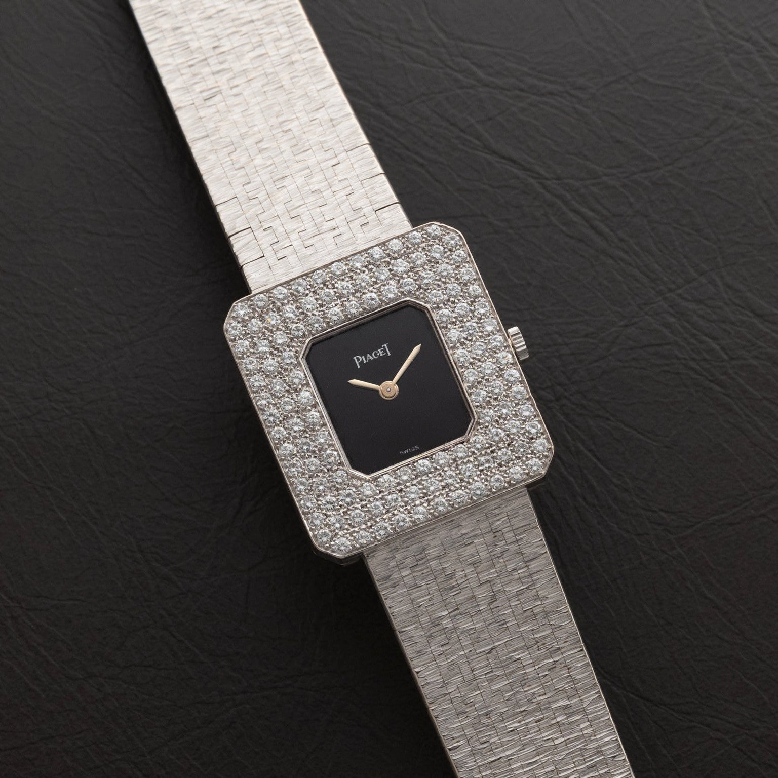 The Piaget Onyx Diamond Dress Watch features a square design with diamond accents and a textured silver band, displayed on black leather.