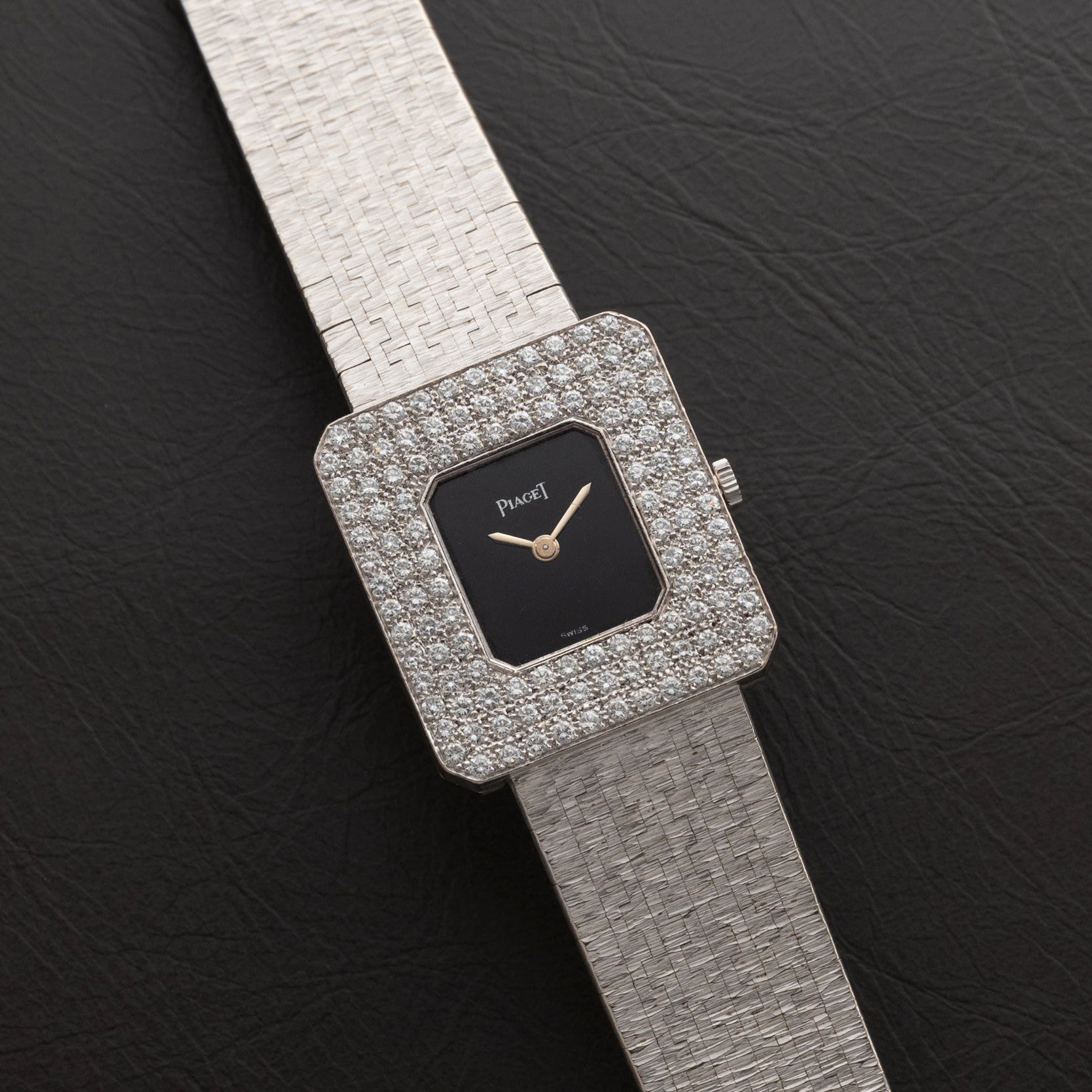 The Piaget Onyx Diamond Dress Watch features a square design with diamond accents and a textured silver band, displayed on black leather.