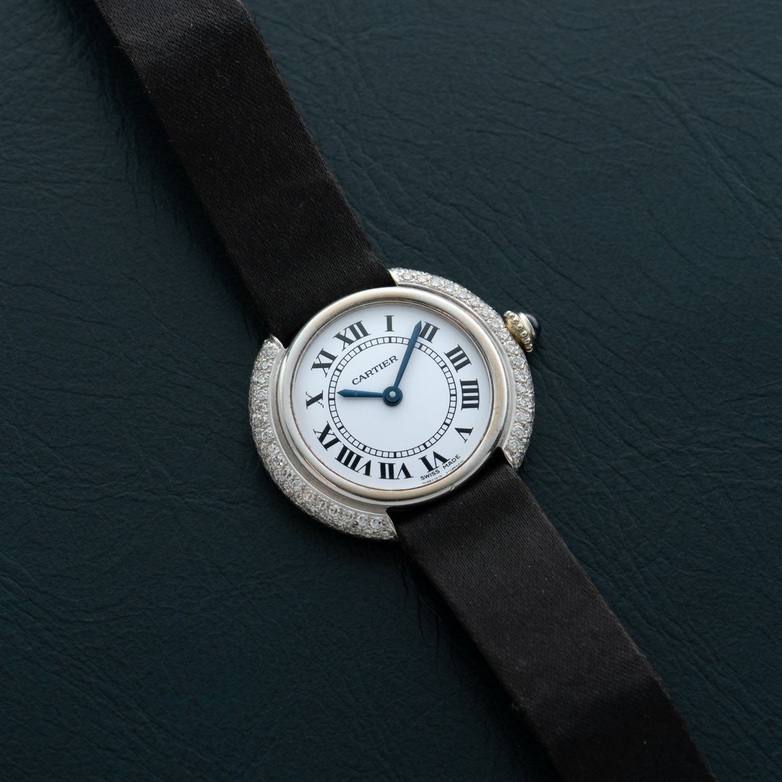 The Cartier Vendome Diamond watch features Roman numerals and a black strap, displayed on a dark textured surface.