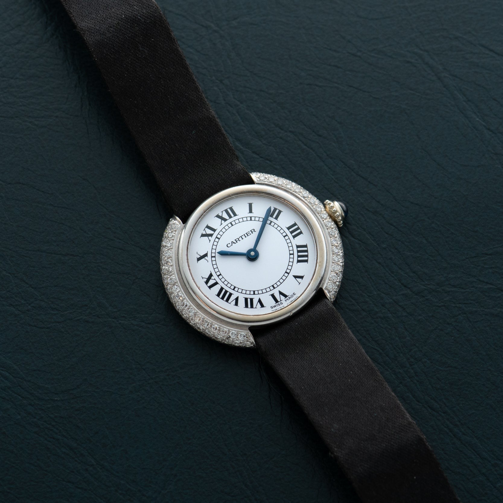 The Cartier Vendome Diamond watch features Roman numerals and a black strap, displayed on a dark textured surface.