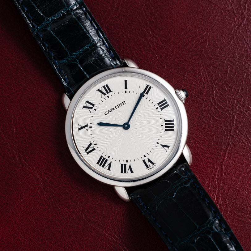 Cartier Vendome Ronde Louis watch with black Roman numerals and a black leather strap, displayed on a dark red leather surface.