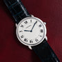Cartier Vendome Ronde Louis watch with black Roman numerals and a black leather strap, displayed on a dark red leather surface.