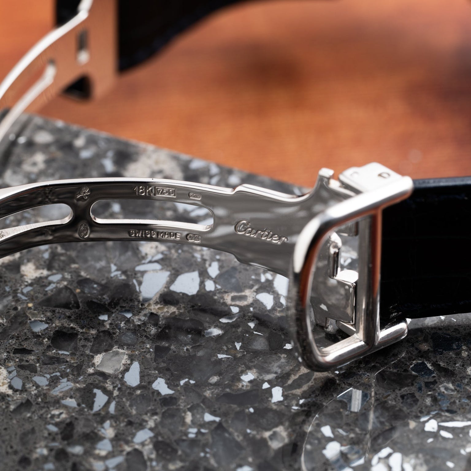 Close-up of a silver Cartier Vendome Ronde Louis watch clasp on a black band, resting on a speckled stone surface.