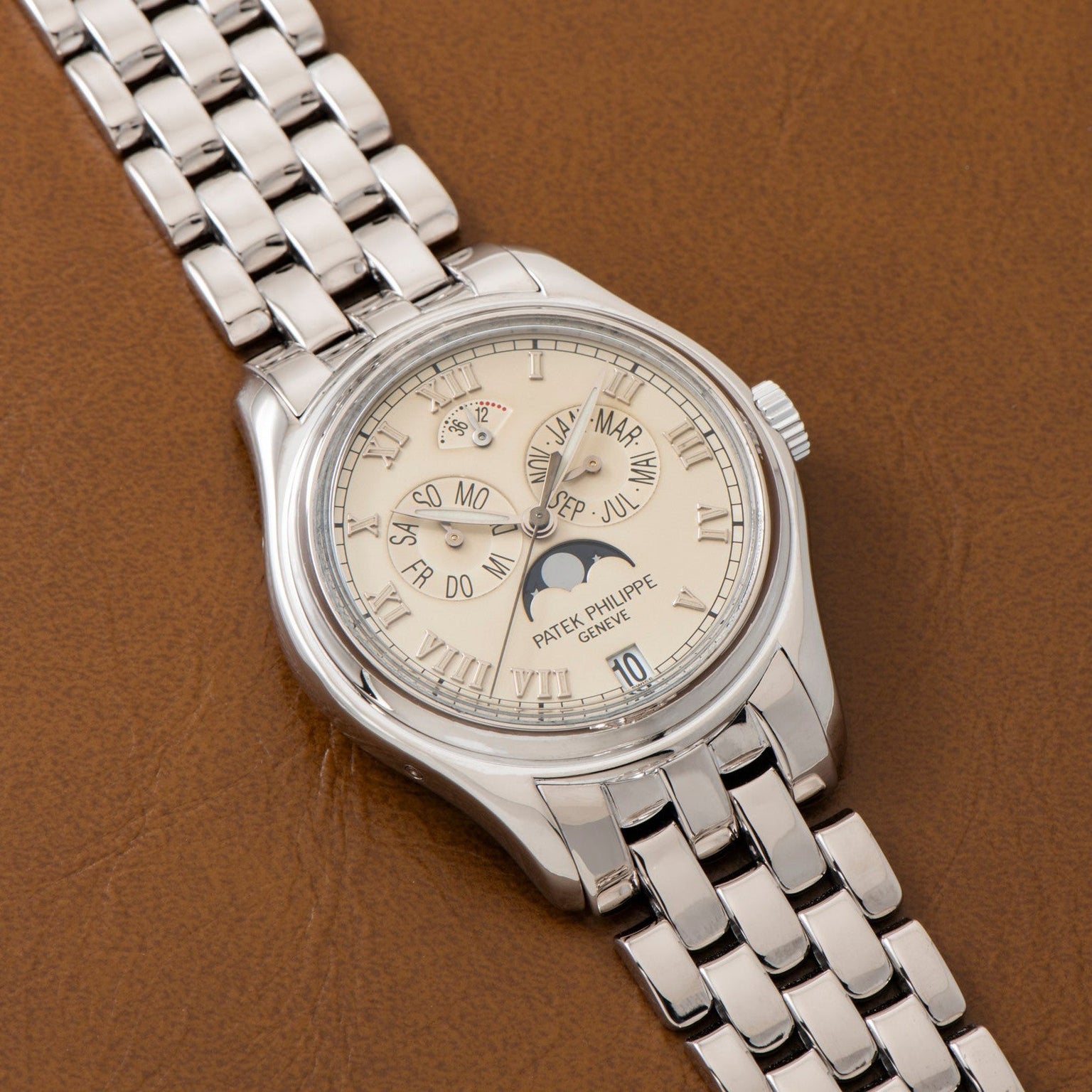 A Patek Philippe Annual Calendar wristwatch in silver with a cream dial and moon phase, displayed on brown leather.