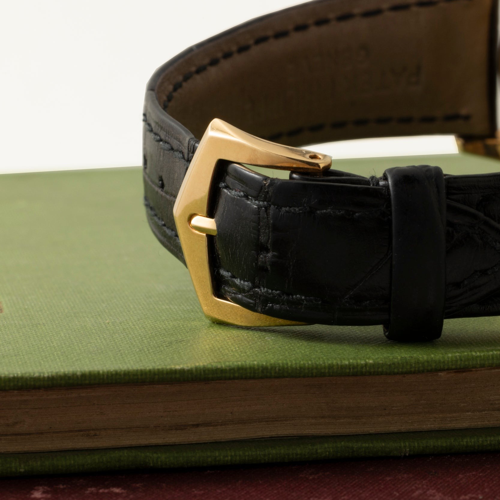 Close-up of the black leather strap with a gold buckle on the Patek Philippe Retrograde Perpetual Calendar watch, resting atop a green hardcover book.
