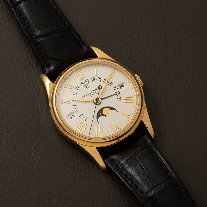 Patek Philippe Retrograde Perpetual Calendar wristwatch with black leather strap, Roman numerals, and moon phase display on a brown surface.
