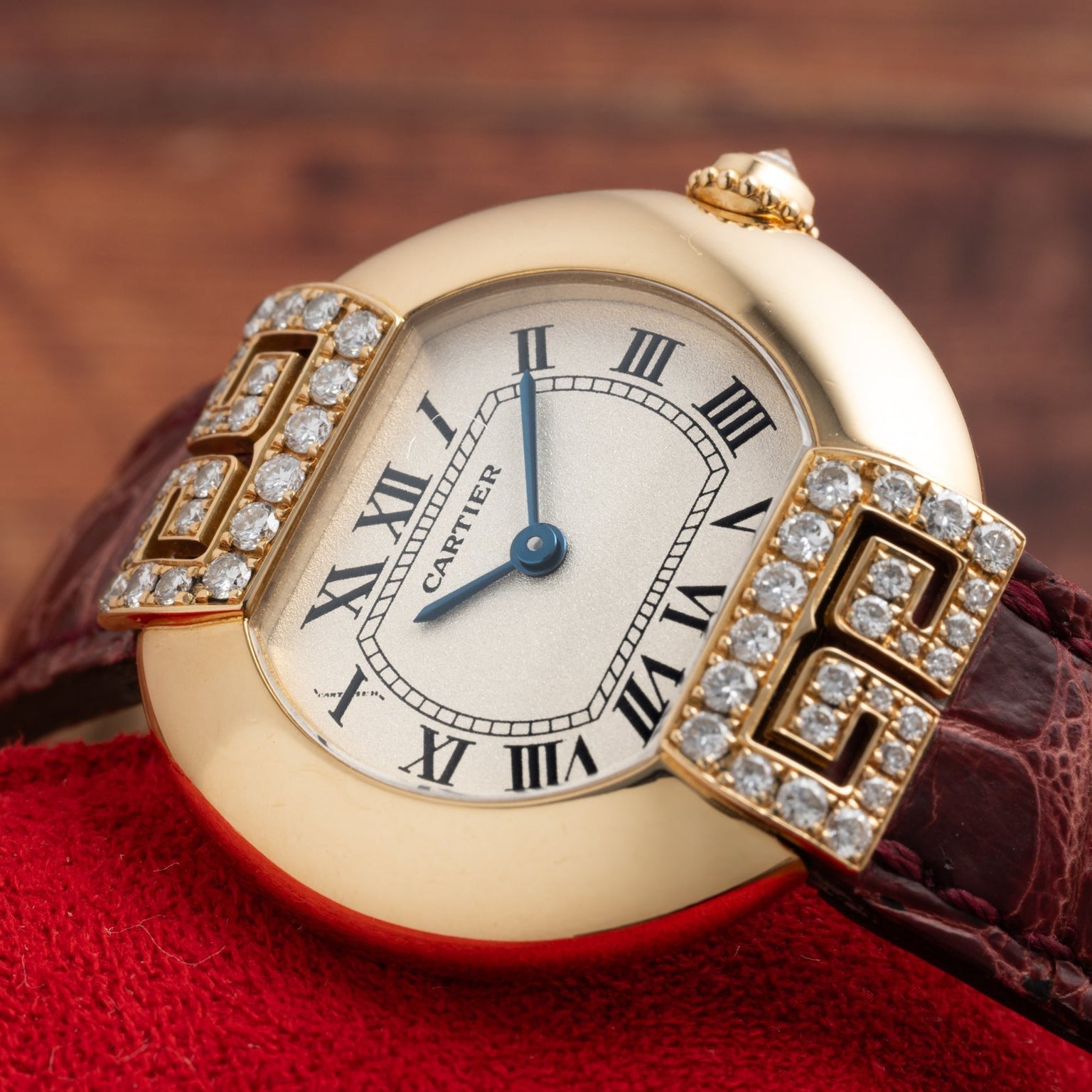 Cartier Ellipse watch featuring a diamond bezel, Roman numerals, and a brown leather strap displayed on a red surface.