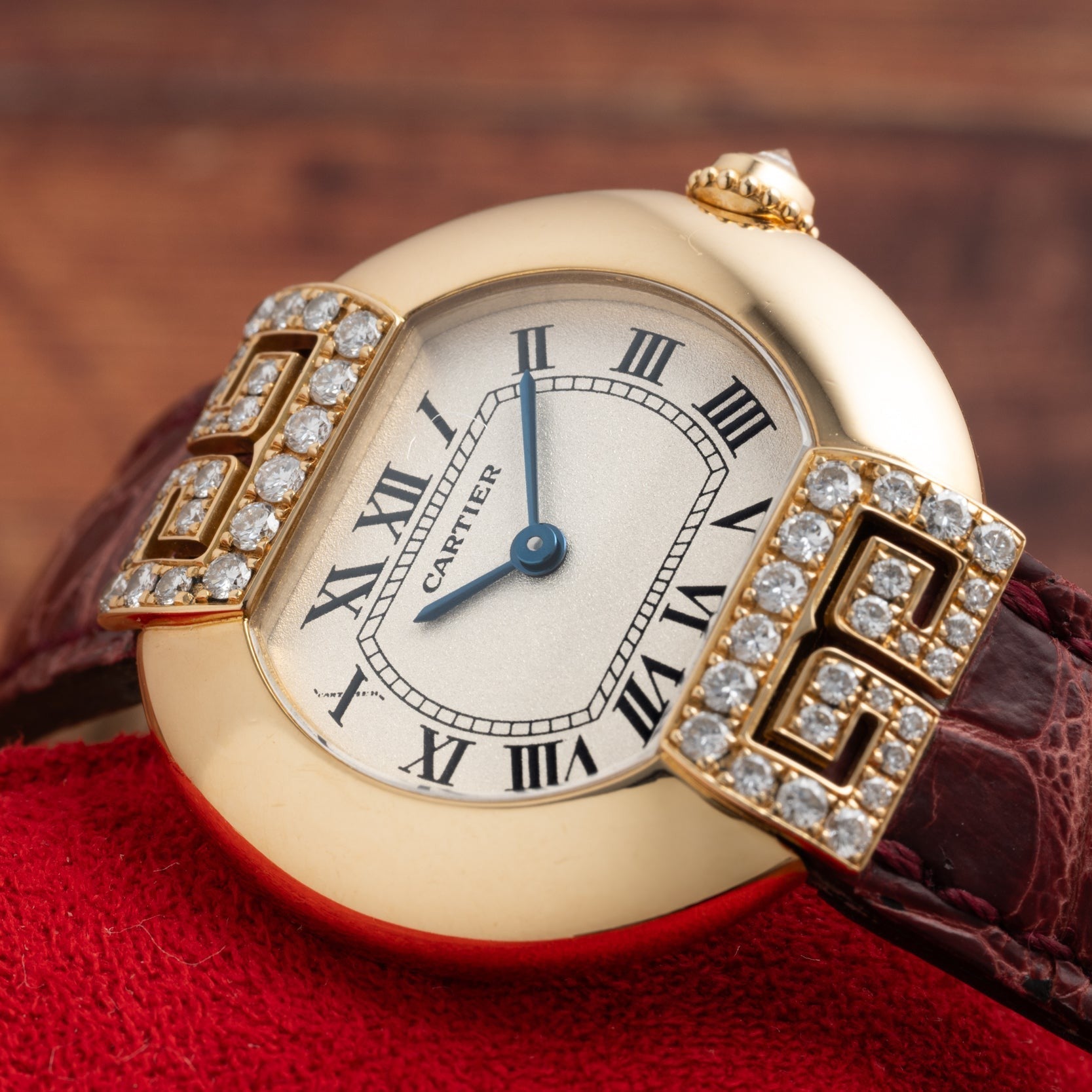 Cartier Ellipse watch featuring a diamond bezel, Roman numerals, and a brown leather strap displayed on a red surface.