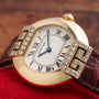Cartier Ellipse watch featuring a diamond bezel, Roman numerals, and a brown leather strap displayed on a red surface.