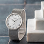 A silver Patek Philippe Calatrava watch with Roman numerals rests on a marble surface against a tiled background.