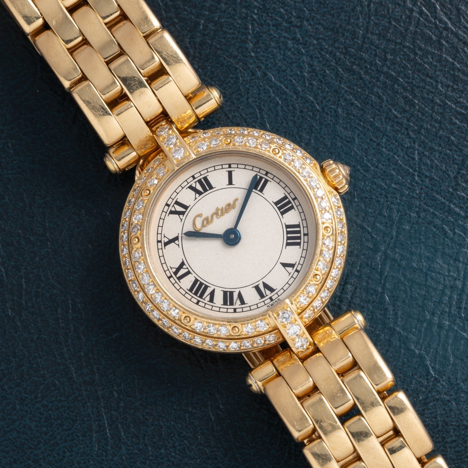 Cartier Panthere Ronde watch with diamond bezel and Roman numeral dial displayed on a dark textured surface.