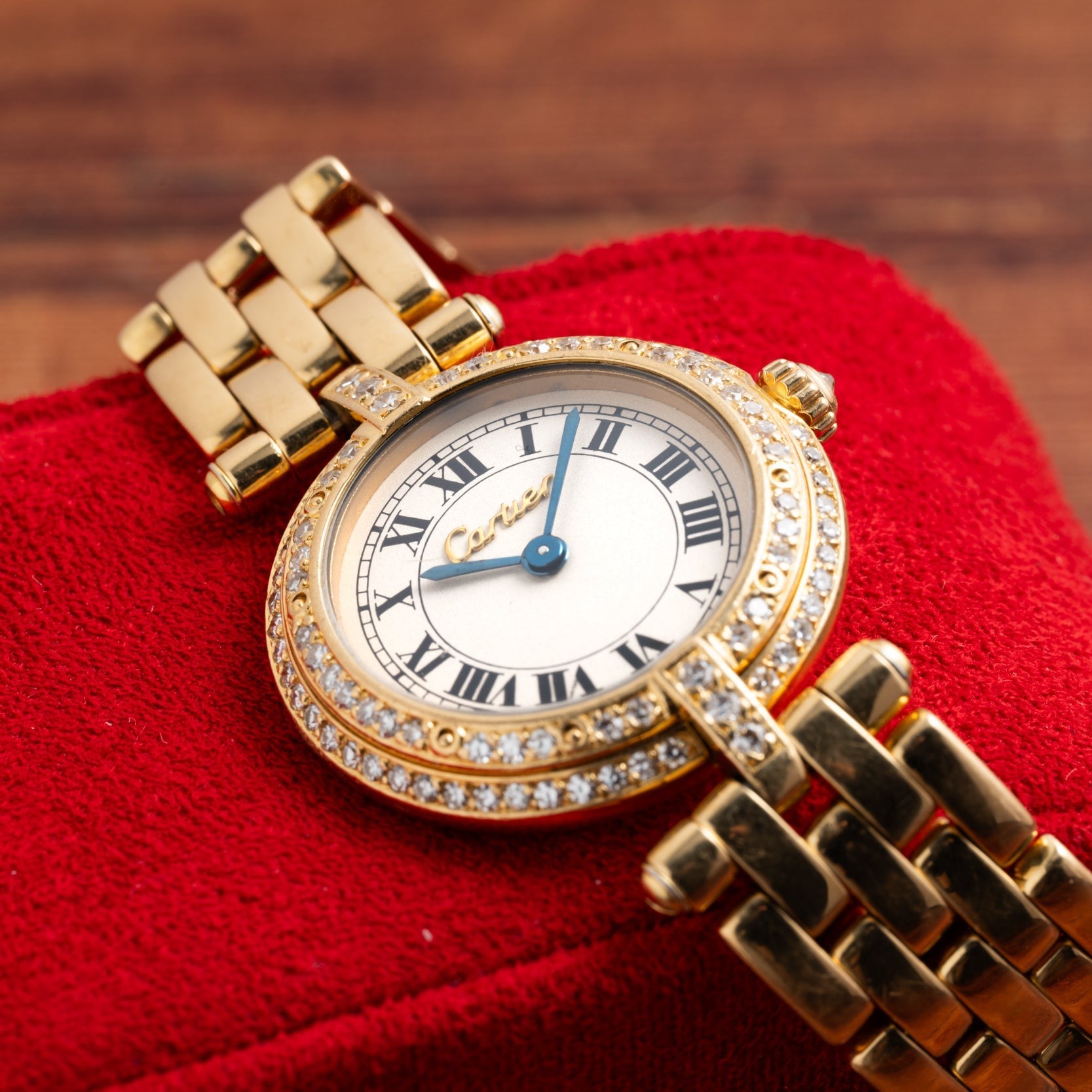 The Cartier Panthere Ronde gold watch with Roman numerals and diamond accents rests on a red textured surface.