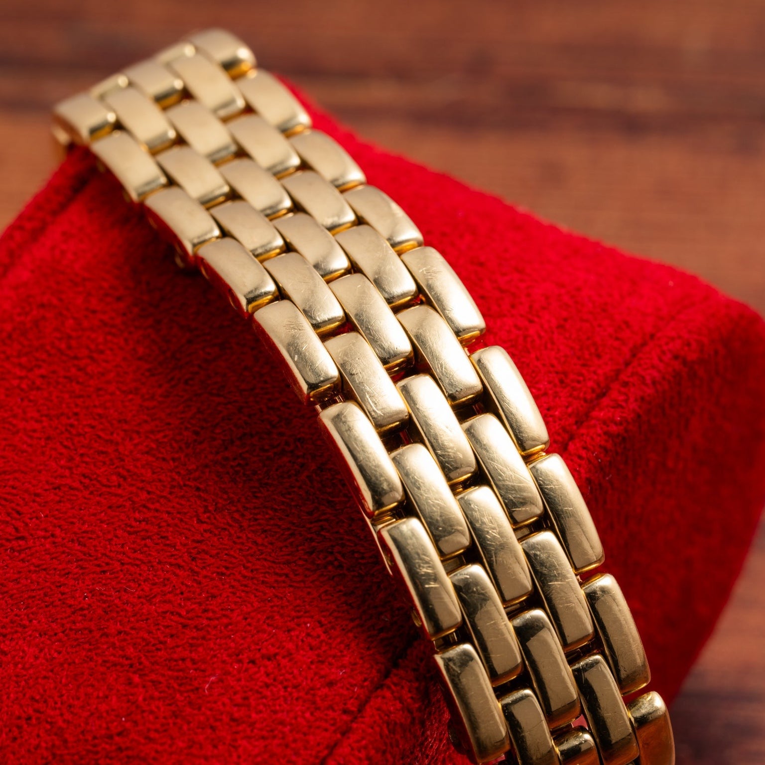 Cartier Panthere Ronde gold metal watch band showcased on a red textured stand with a wooden background.