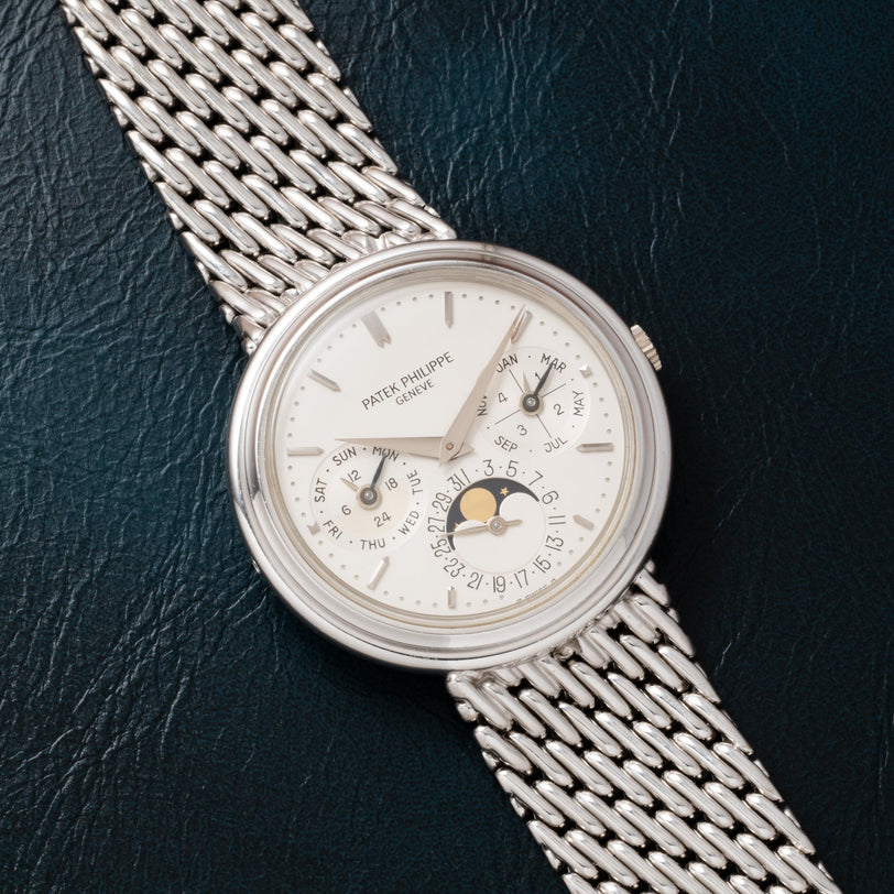 A Patek Philippe Perpetual Calendar watch with a silver metal band rests on a dark textured surface.