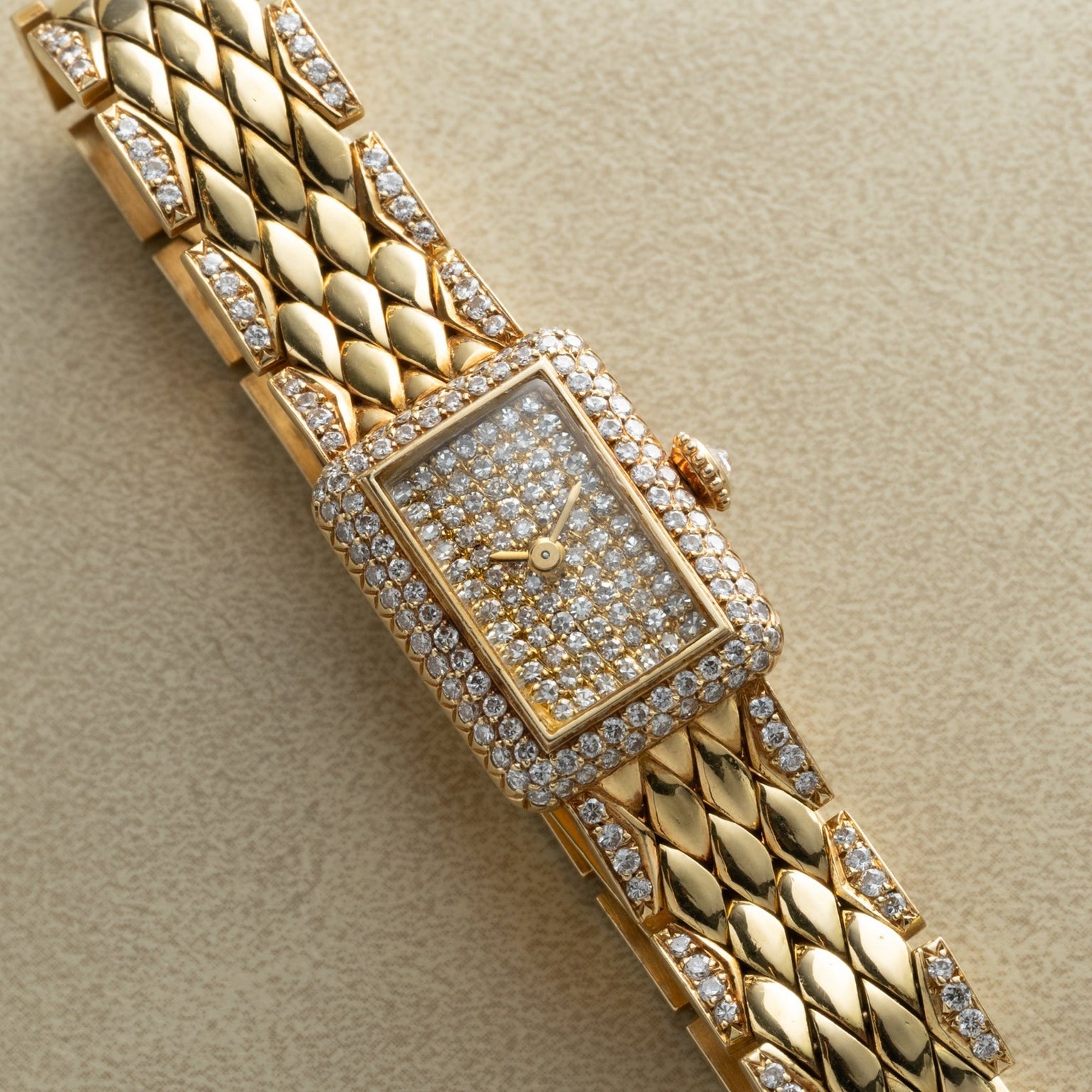 Cartier Tank Mini Diamond wristwatch featuring a rectangular diamond-encrusted face and band, displayed on a beige surface.