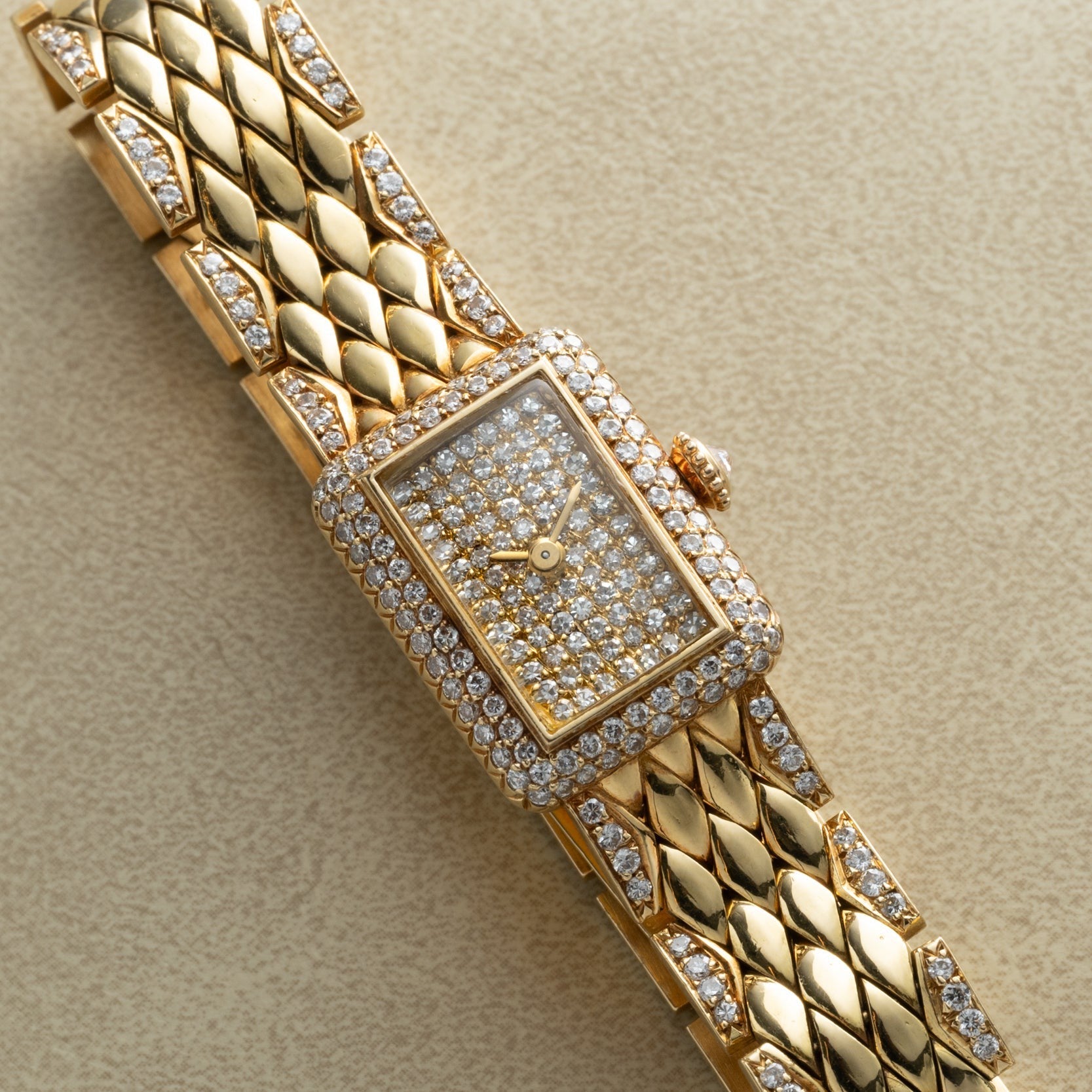 Cartier Tank Mini Diamond wristwatch featuring a rectangular diamond-encrusted face and band, displayed on a beige surface.