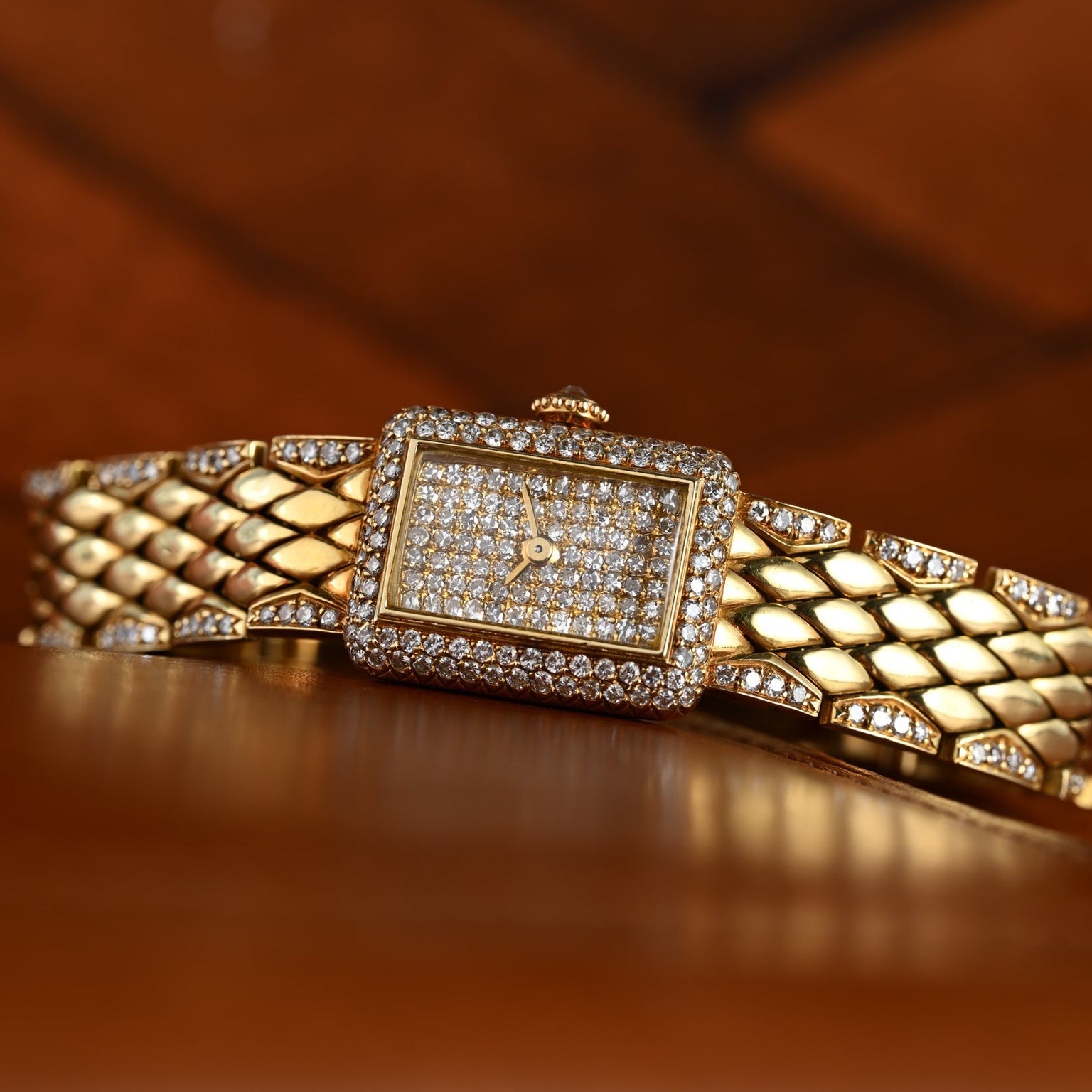 The Cartier Tank Mini Diamond wristwatch, featuring a diamond-encrusted face and band, rests on a wooden surface.