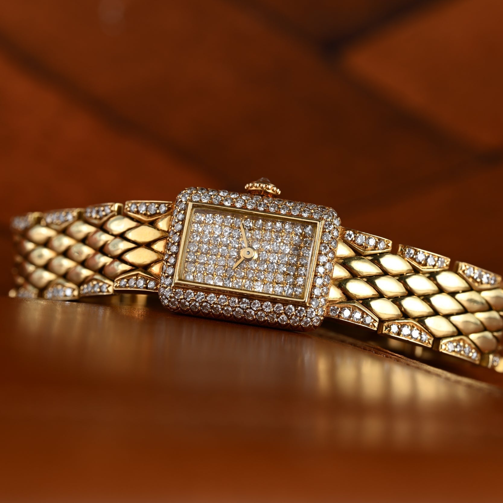 The Cartier Tank Mini Diamond wristwatch, featuring a diamond-encrusted face and band, rests on a wooden surface.