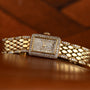 The Cartier Tank Mini Diamond wristwatch, featuring a diamond-encrusted face and band, rests on a wooden surface.