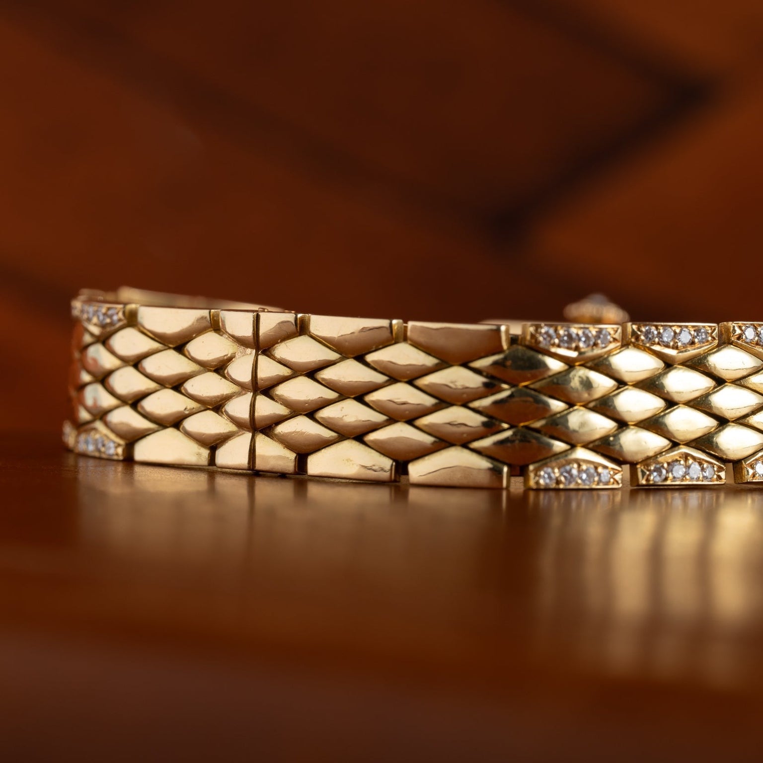 A close-up of the Cartier Tank Mini Diamond gold bracelet, featuring a diamond pattern with small diamonds, displayed on a wooden surface.