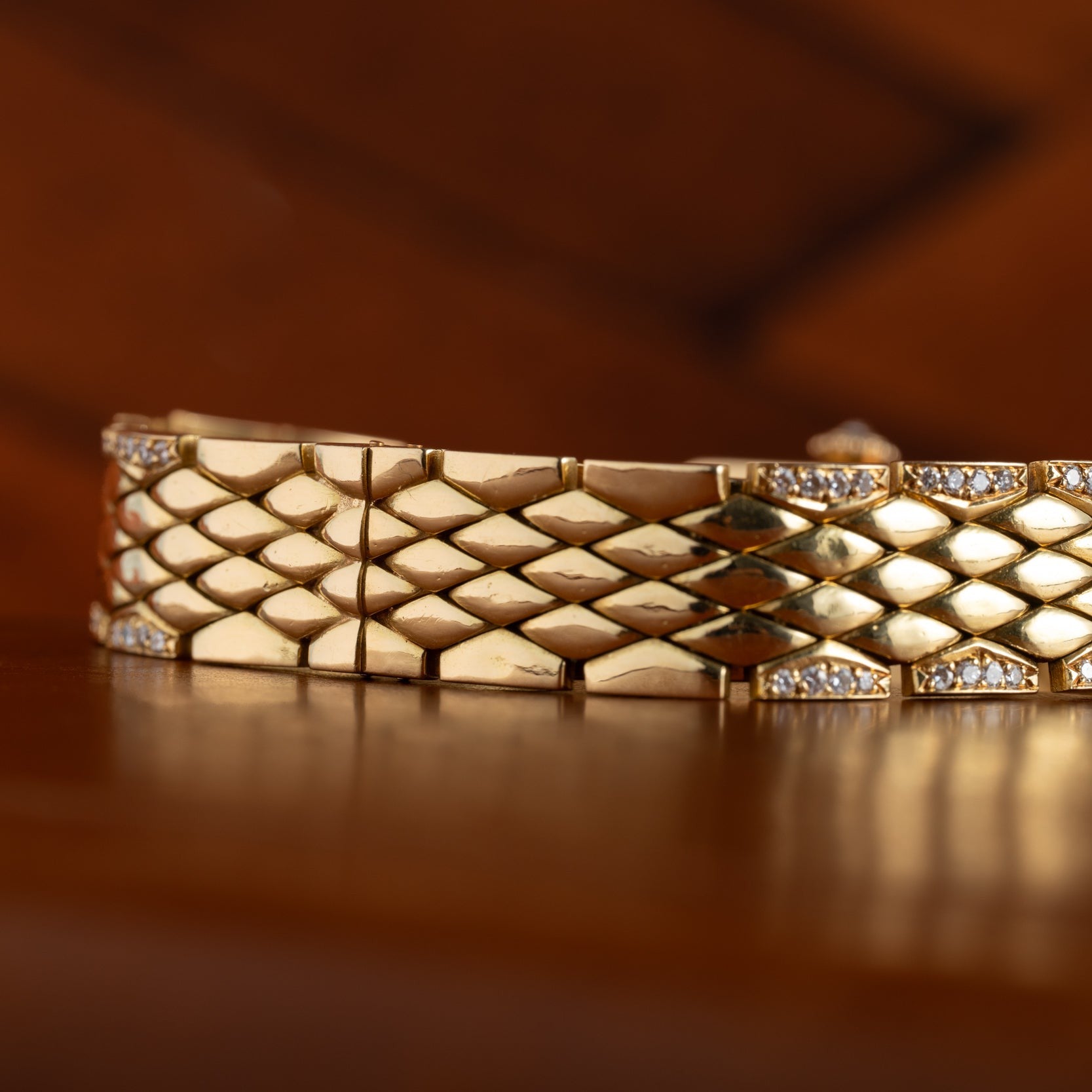 A close-up of the Cartier Tank Mini Diamond gold bracelet, featuring a diamond pattern with small diamonds, displayed on a wooden surface.