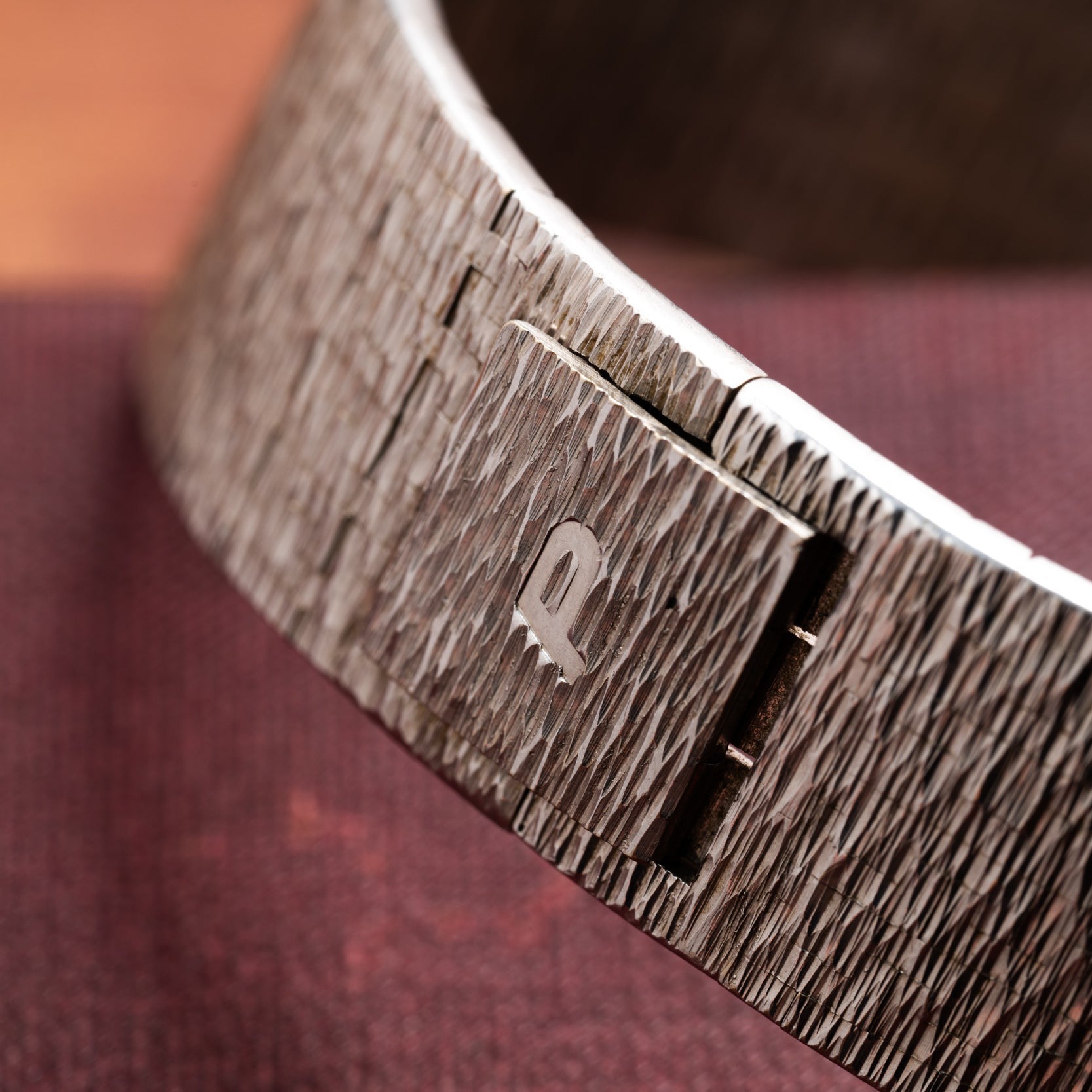 Close-up of the Piaget White Gold Lapis Lazuli Dress Watch featuring a textured band and metallic logo, displayed on maroon fabric.