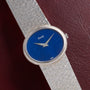 A Piaget White Gold Lapis Lazuli Dress Watch with a blue face rests on a dark red leather surface.