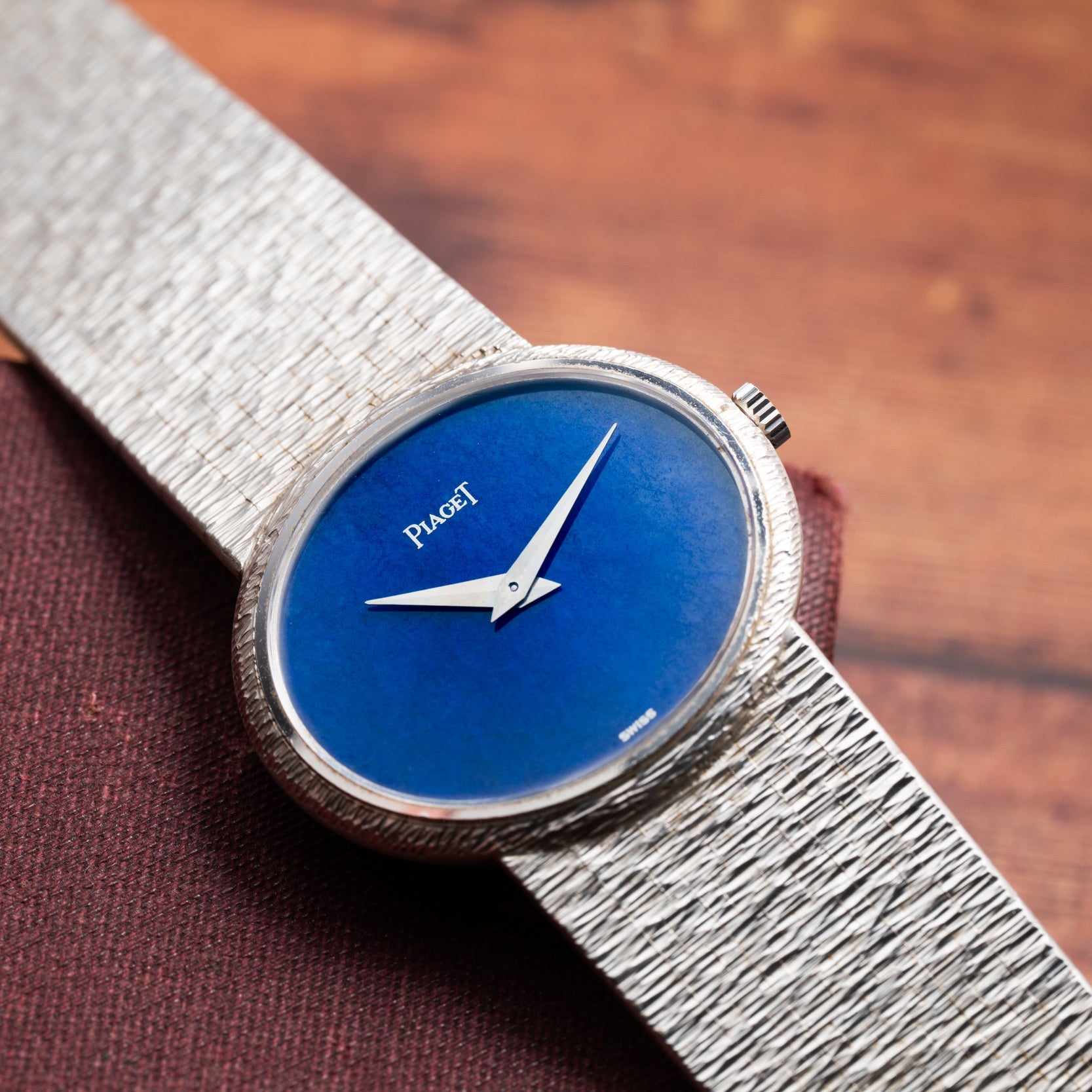 A Piaget White Gold Lapis Lazuli Dress Watch featuring a blue face rests on a brown wooden surface.