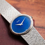 A Piaget White Gold Lapis Lazuli Dress Watch featuring a blue face rests on a brown wooden surface.