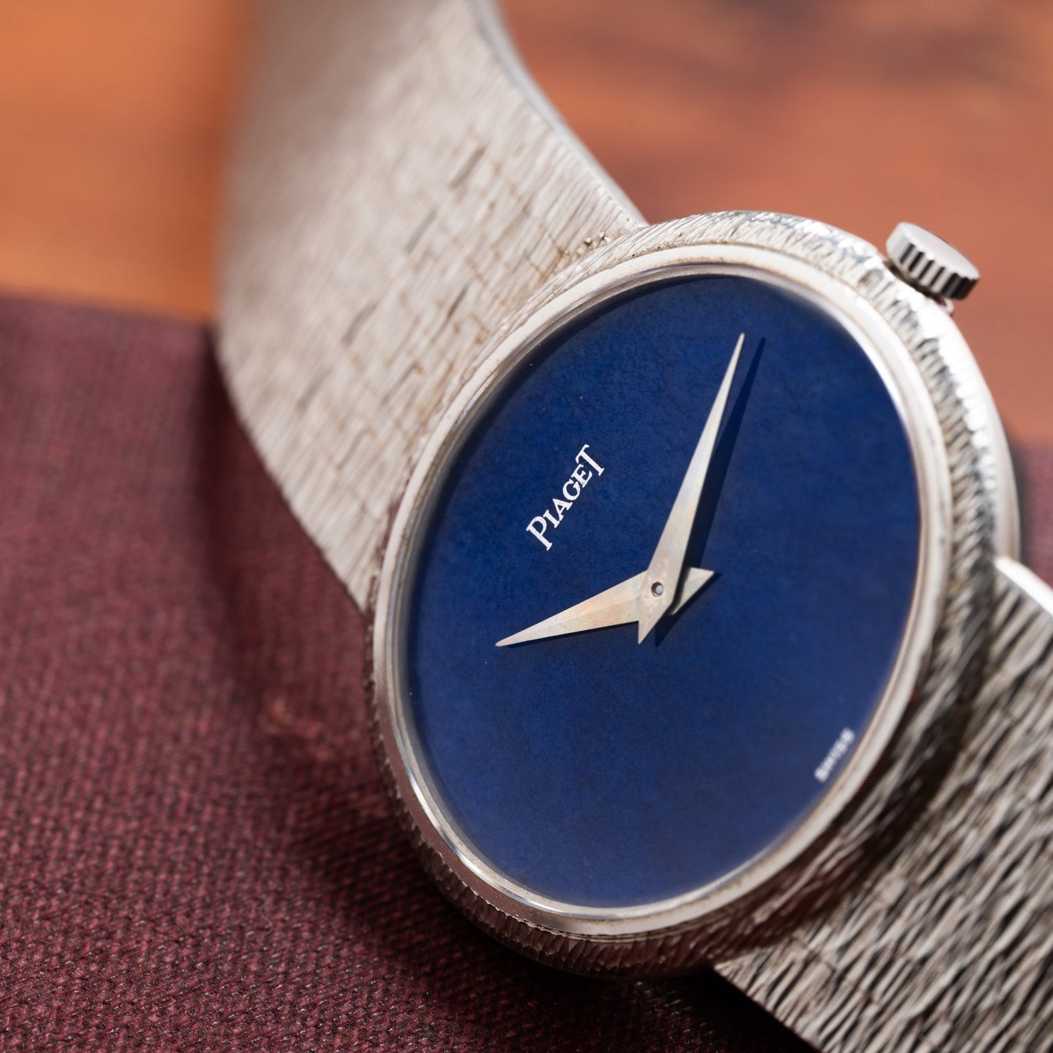 A close-up of a Piaget White Gold Lapis Lazuli Dress Watch with a blue lapis lazuli face and textured silver band on a brown surface.
