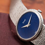 A close-up of a Piaget White Gold Lapis Lazuli Dress Watch with a blue lapis lazuli face and textured silver band on a brown surface.