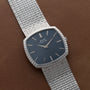 A Piaget Sqound White Gold Dress Watch with a textured band and black dial, displayed on a brown leather surface.