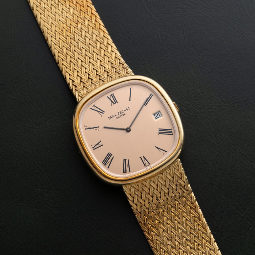 Patek Philippe Ellipse Jumbo watch with Roman numerals on a woven gold band, displayed on a black surface.