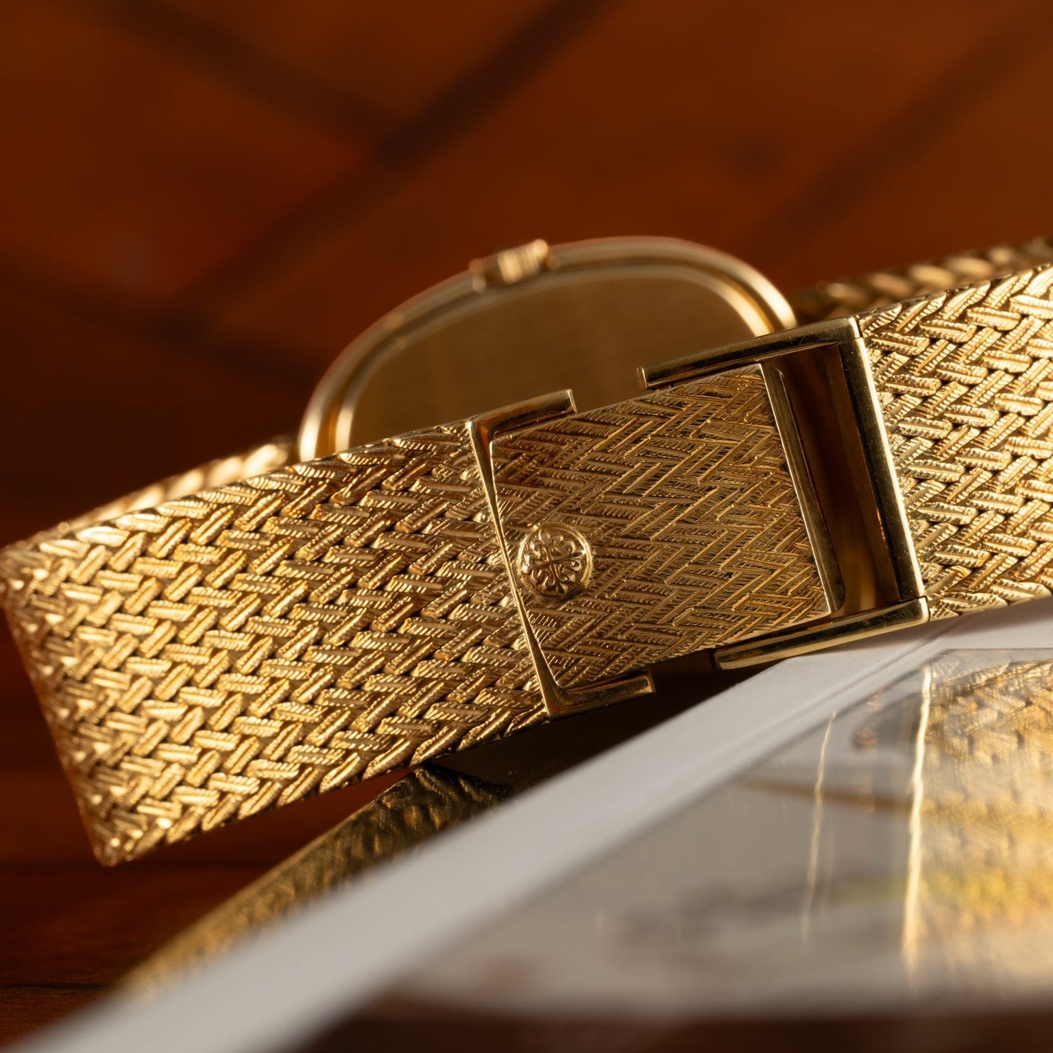 Close-up of the Patek Philippe Ellipse Jumbo gold wristwatch with a textured band, resting on a glossy magazine surface.