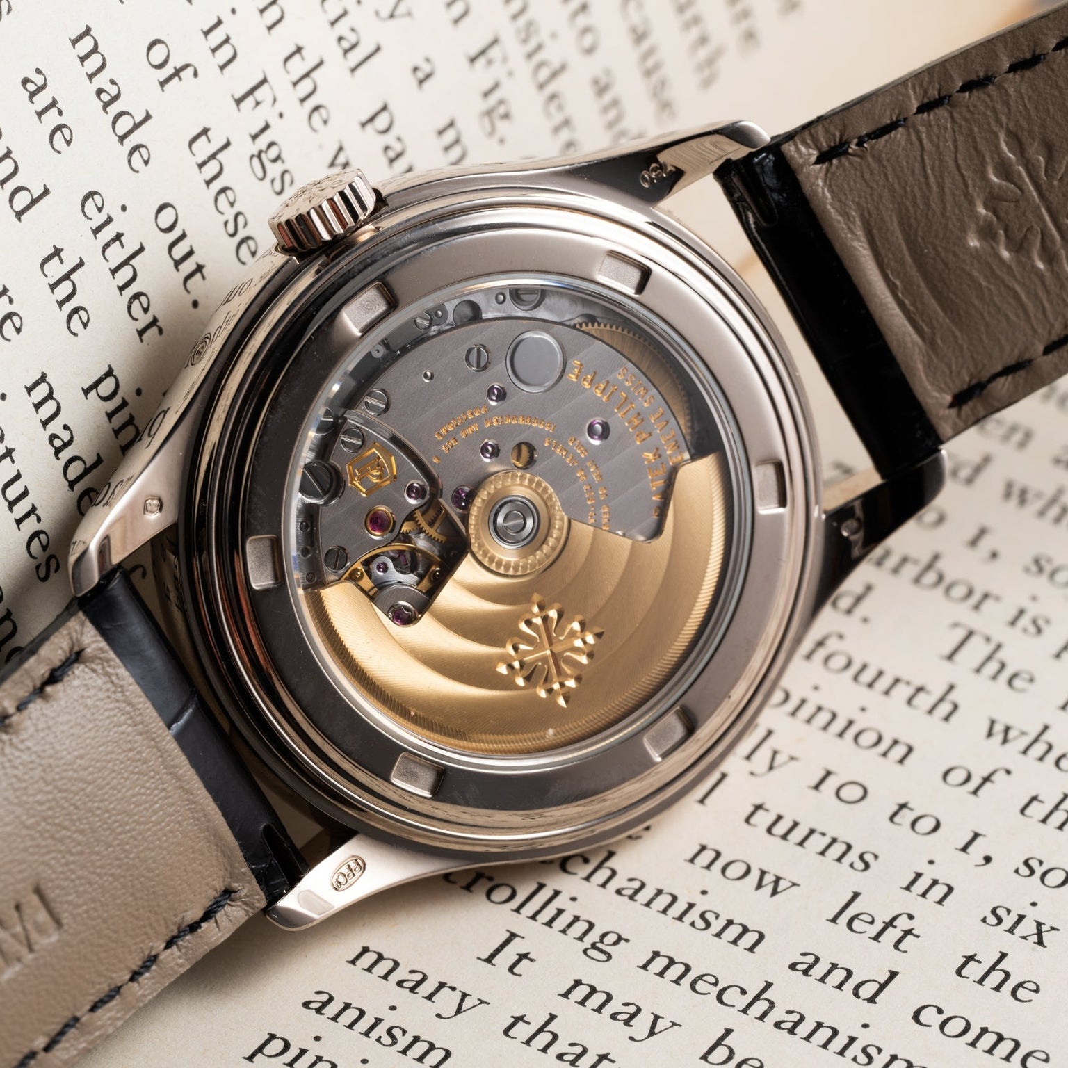 Close-up of a Patek Philippe Annual Calendar Moonphase watch’s exposed movement, resting on an open book with visible text.