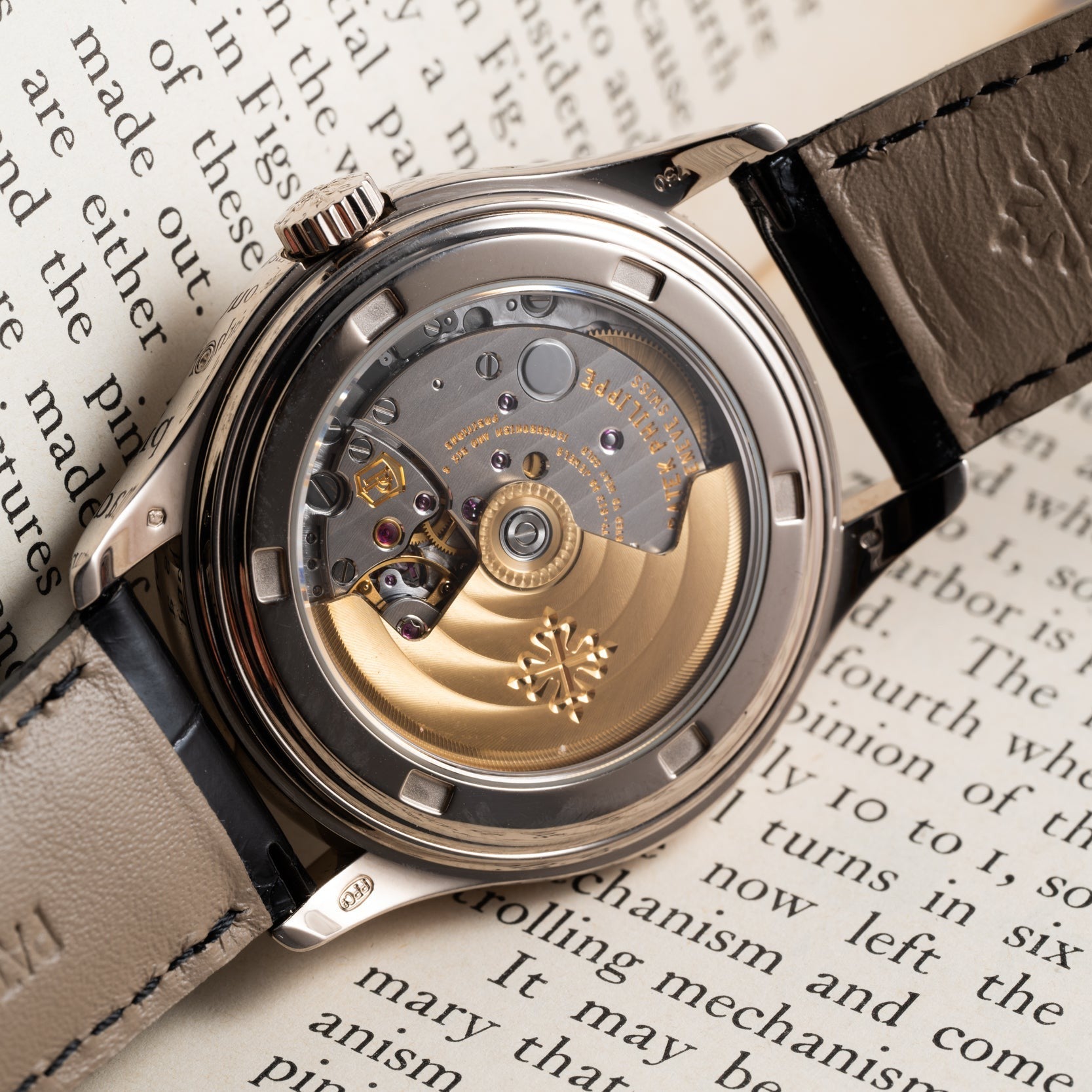 Close-up of a Patek Philippe Annual Calendar Moonphase watch’s exposed movement, resting on an open book with visible text.