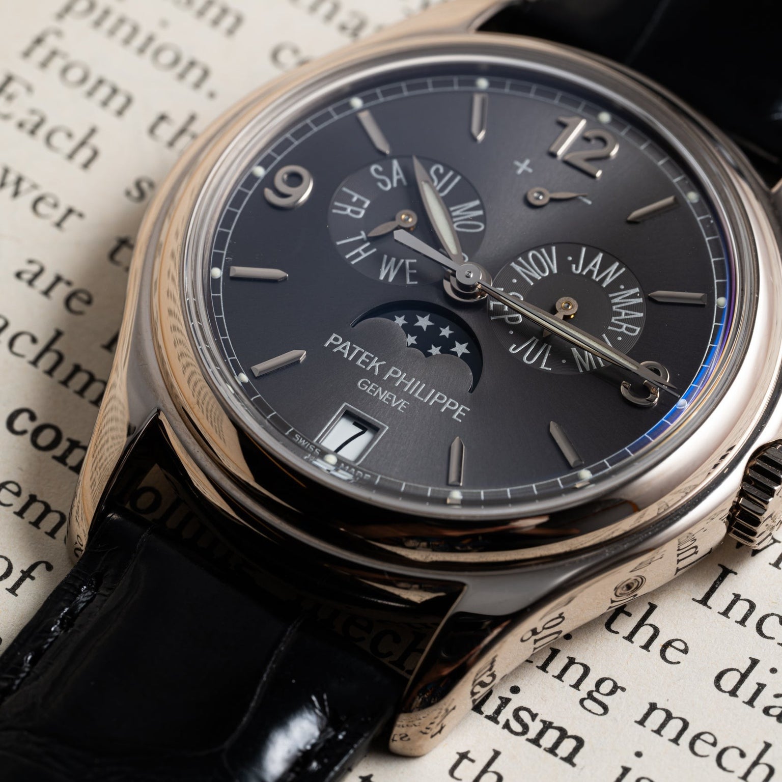 The Patek Philippe Annual Calendar Moonphase watch with a black strap rests on an open book.
