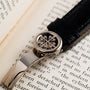 A Patek Philippe Annual Calendar Moonphase watch clasp, featuring a cross-like logo, rests on an open book with visible text.