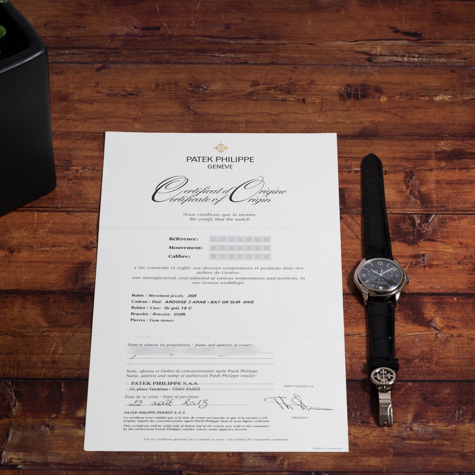 A Patek Philippe Annual Calendar Moonphase wristwatch and certificate of origin displayed on a wooden surface.