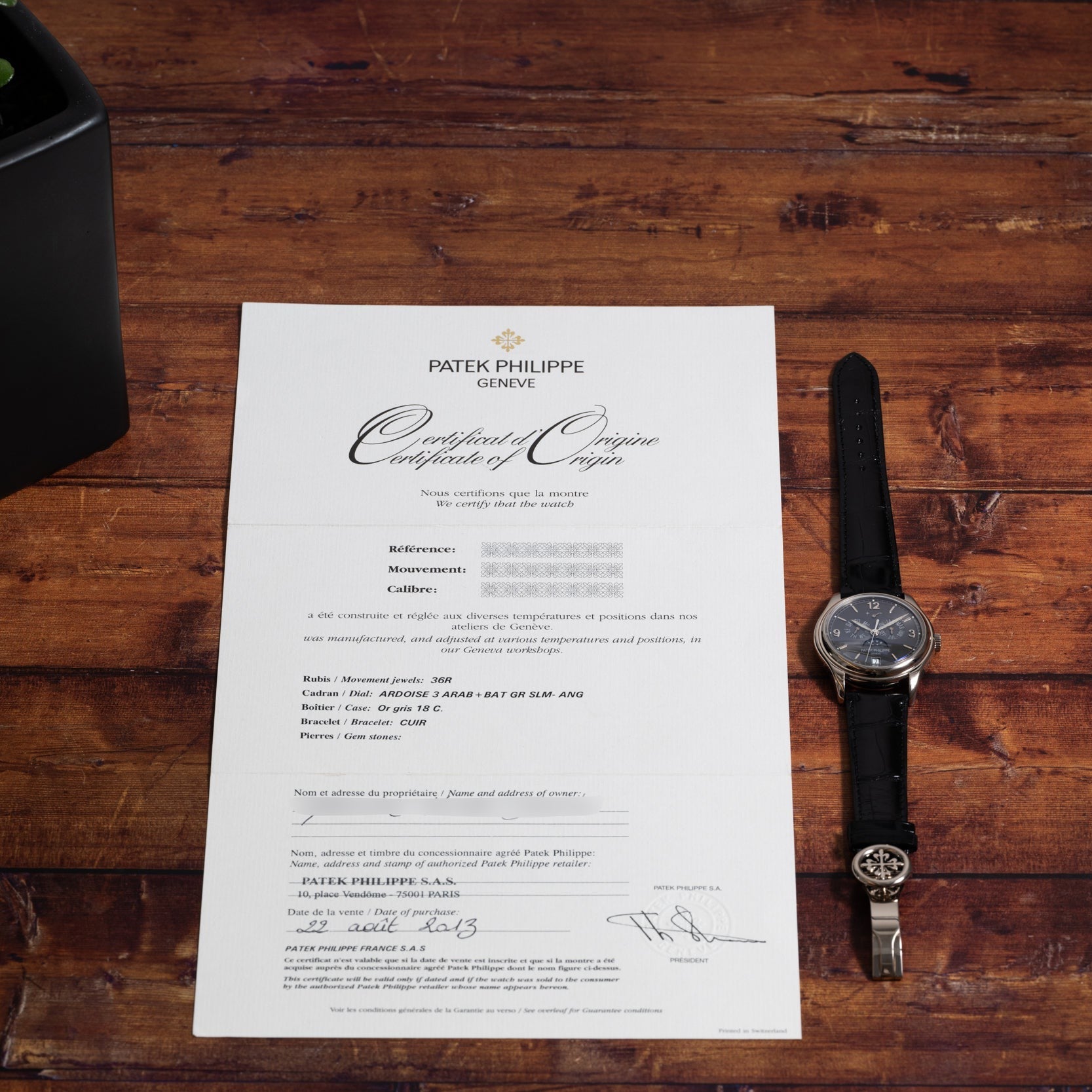 A Patek Philippe Annual Calendar Moonphase wristwatch and certificate of origin displayed on a wooden surface.