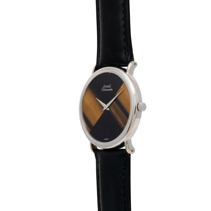 The Piaget Tigers Eye Onyx Dress Watch features an oval silver case, black leather strap, and a geometric two-tone brown and black dial.