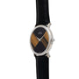 The Piaget Tigers Eye Onyx Dress Watch features an oval silver case, black leather strap, and a geometric two-tone brown and black dial.