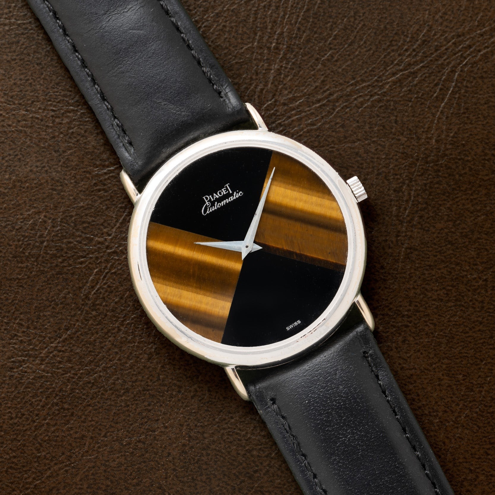 The Piaget Tigers Eye Onyx Dress Watch features a black leather strap and a brown-and-black striped dial, shown resting on a brown leather surface.